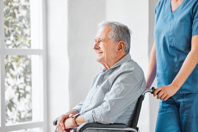 Man with gray hair in a wheelchair looking at a window and smiling