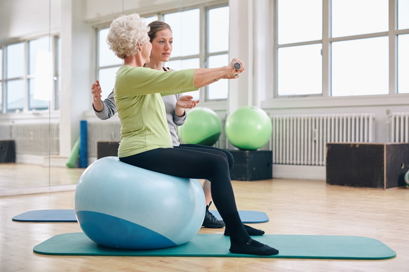 Lady with gray hair excersising and lifting weight with a coach
